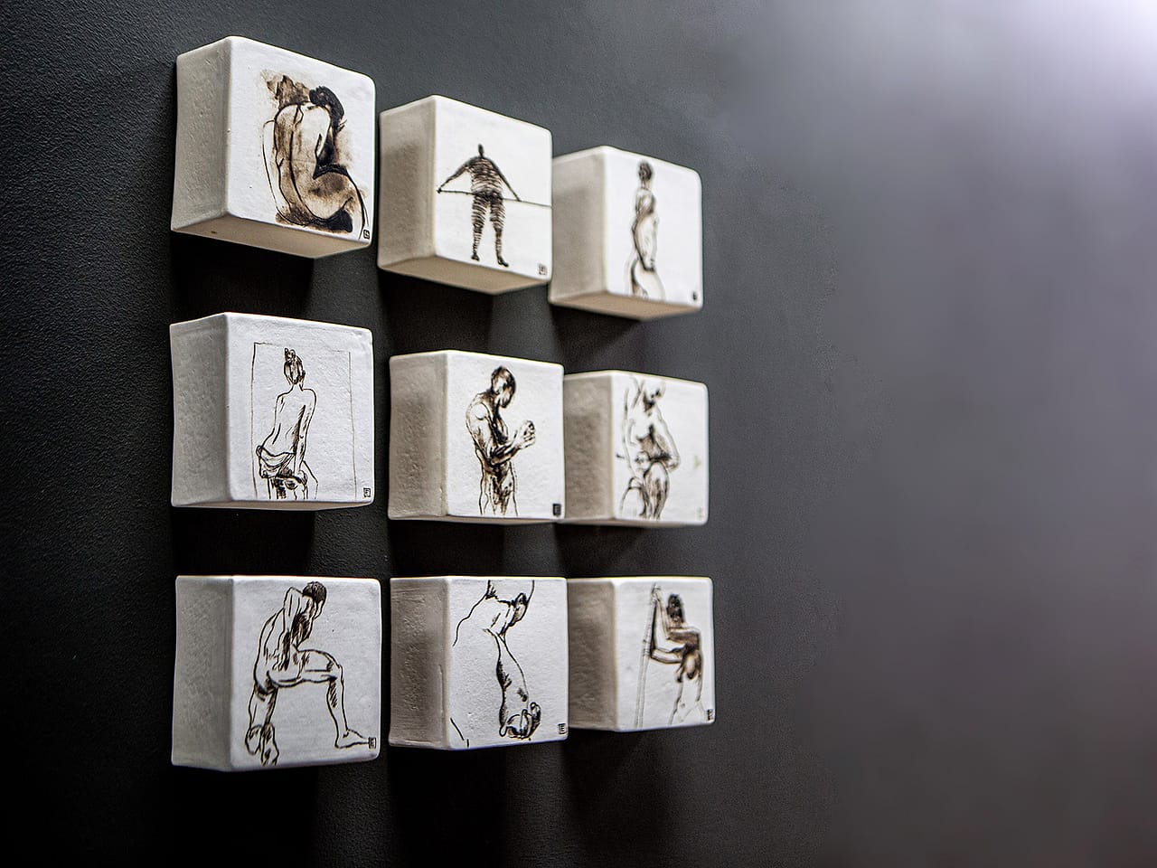 Figure studies drawn on a grid of white ceramic blocks mounted on a dark wall in the practice.