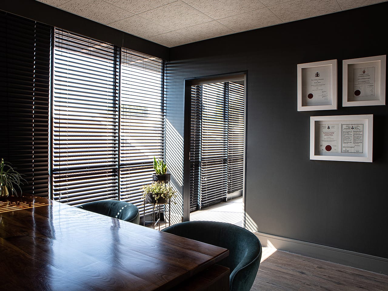 A long timber meeting table beside floor-to-ceiling blinds, where the care team reviews cases together.