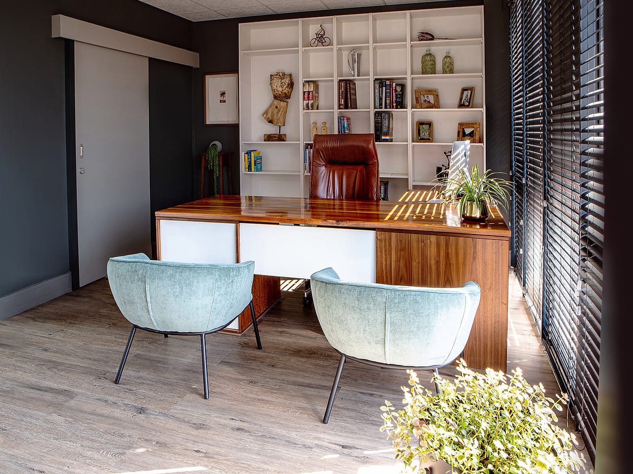 A consulting room with a walnut desk, pale blue armchairs and a full wall of bookshelves.
