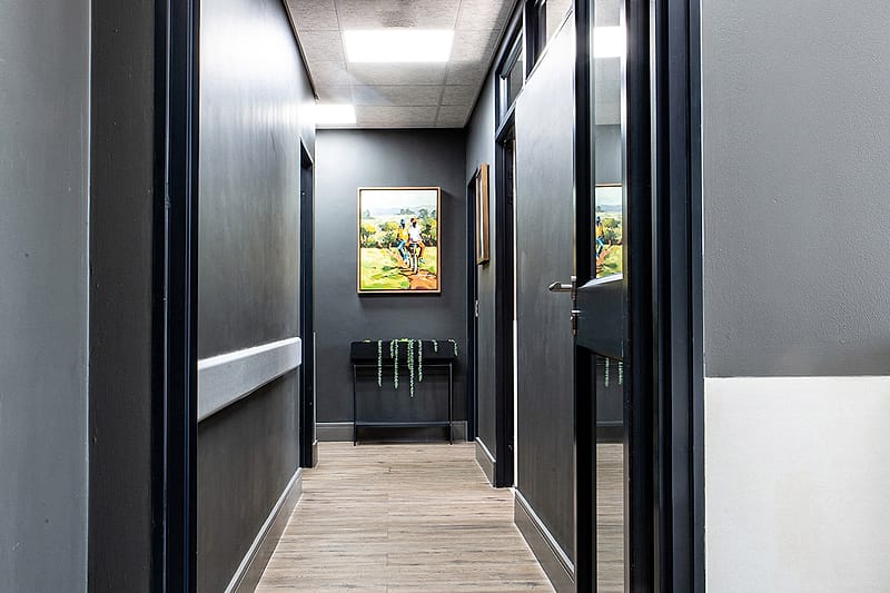 The corridor between the consulting rooms, a painting lit at the far end.