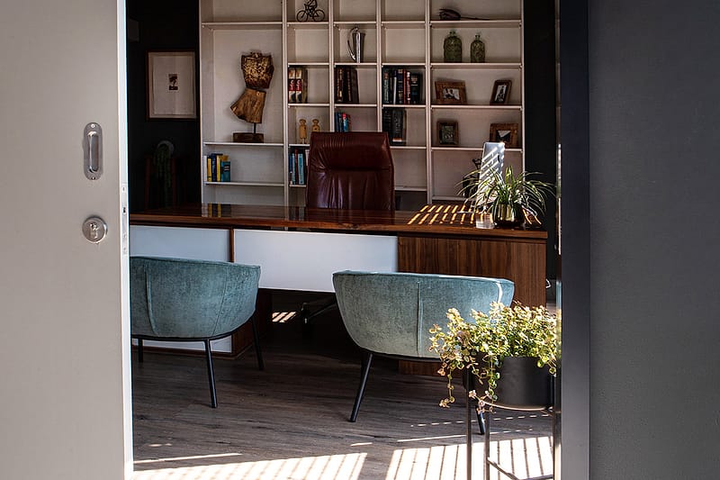 A consulting room seen through its open door, two armchairs beside a bookshelf.