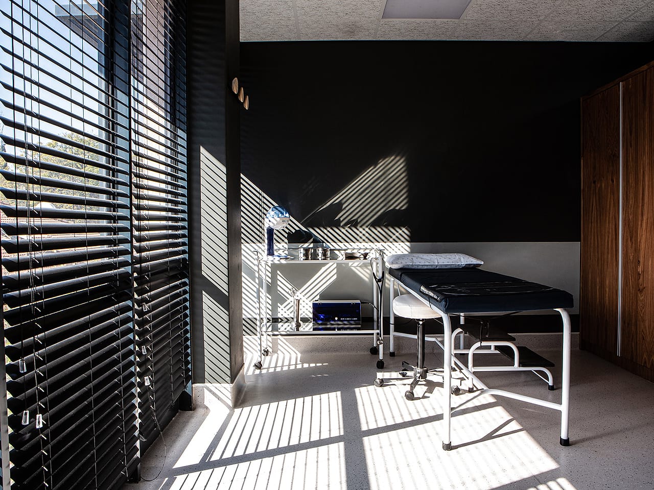 An examination room with an examination couch beside a window with timber blinds.