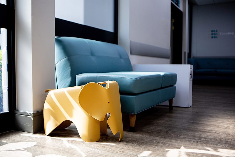 A yellow moulded elephant stool beside a teal couch in a hospital lounge.