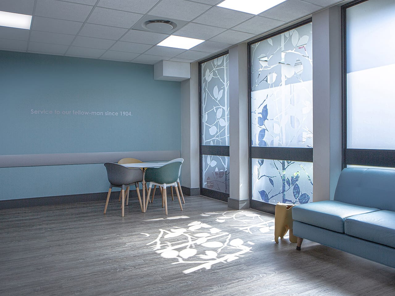 A family room on the ward, sunlight falling through patterned window film onto a small table.