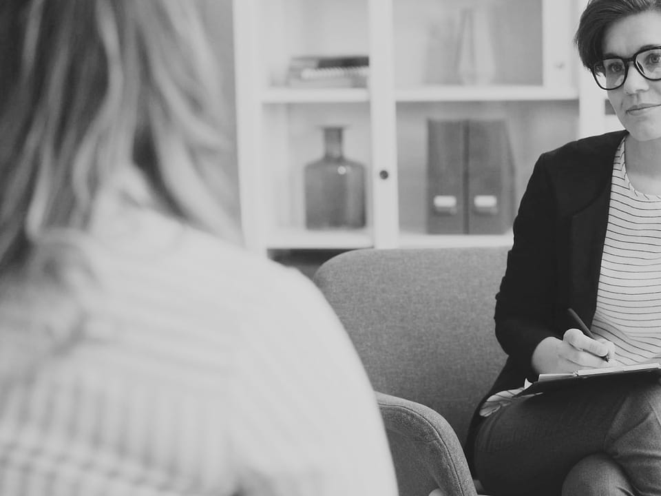 A black-and-white photo of a counsellor listening to a patient.